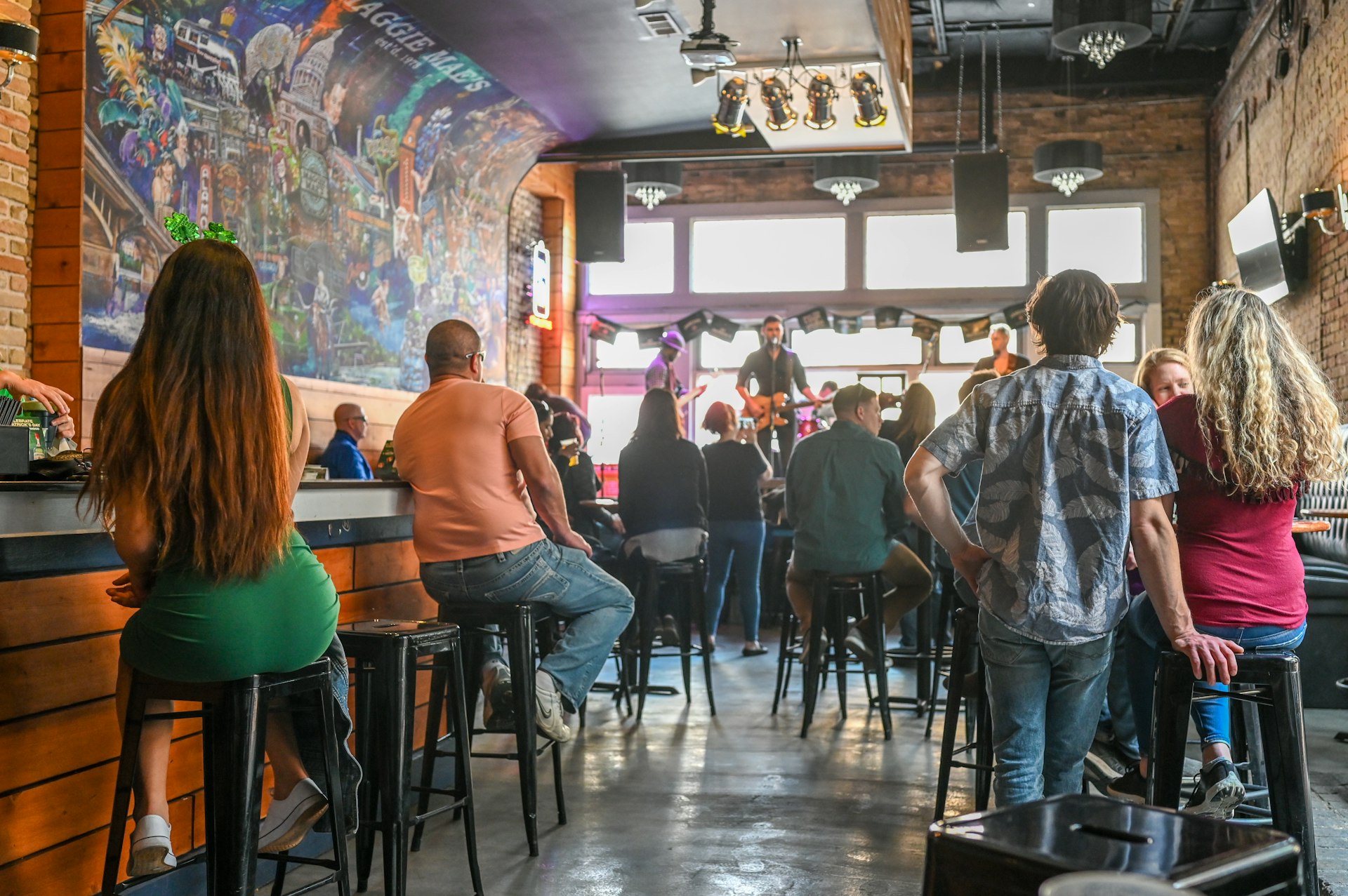 People gather in a bar to listen to live music being performed by a band on a stage at the front