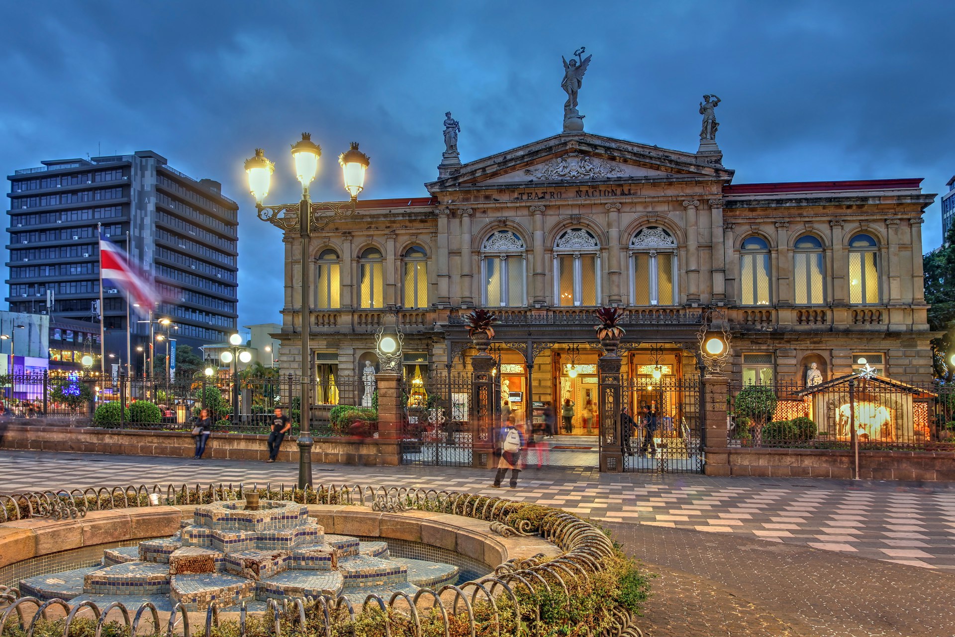 People walking through the square in front of the famous neoclassical National Theater of Costa Rica in San Jose at night.