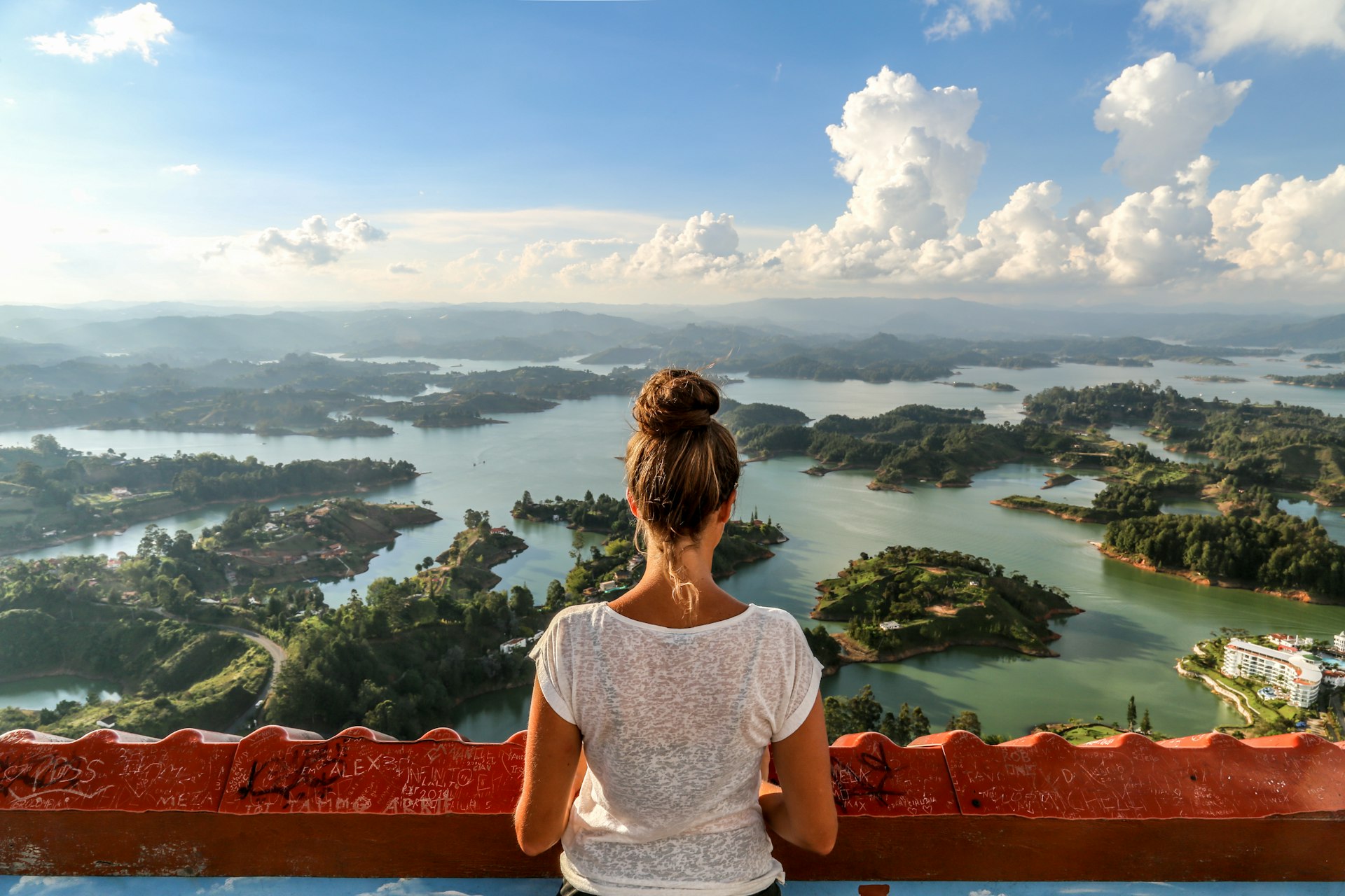 A girl seen from behind, looking out over Guatape and the expansive lake system.