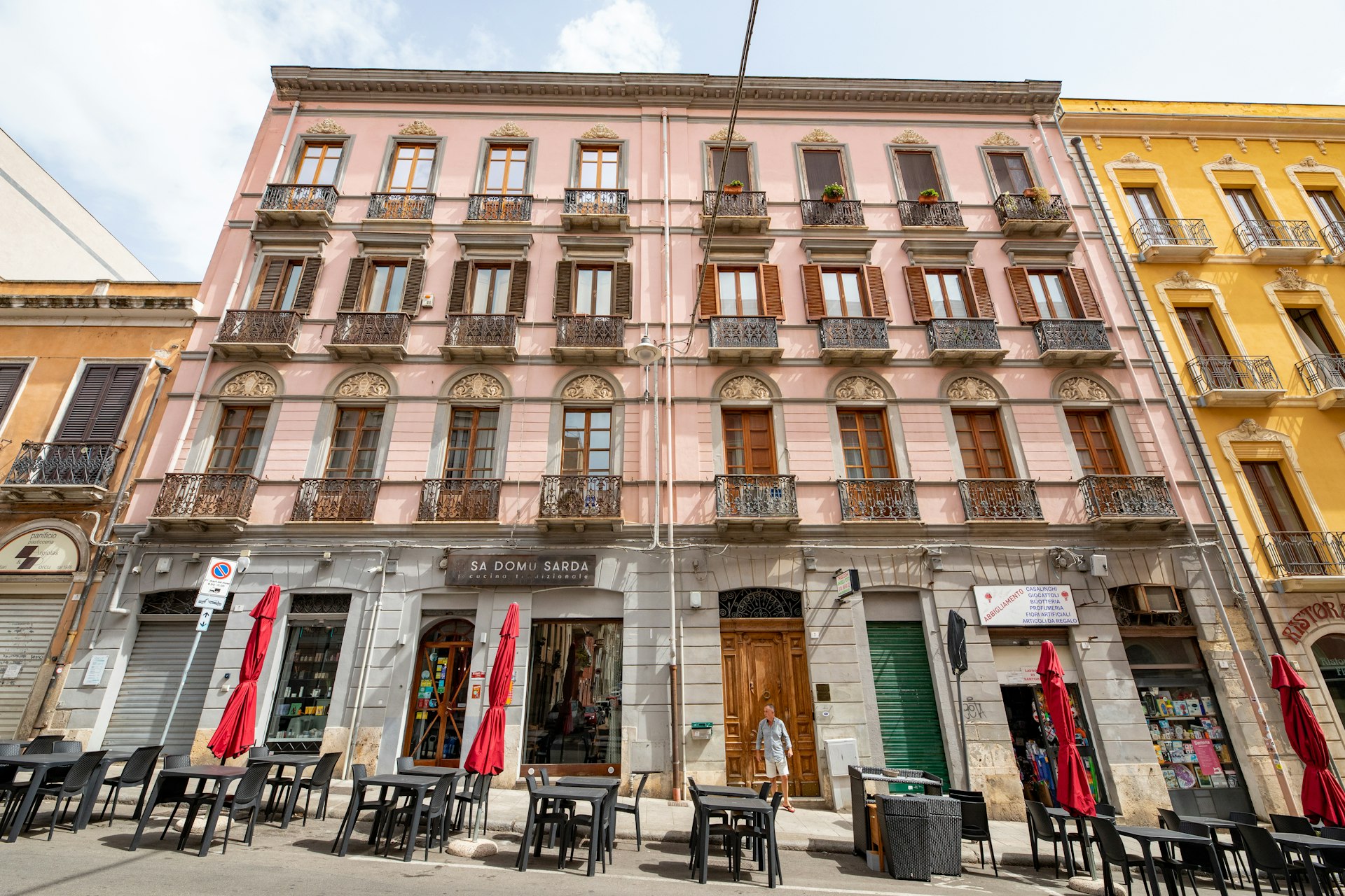 A traditional Sardinian restaurant in the heart of Cagliari – four floors, painted light pink, lots of windows with terraces above, and tables outside the building