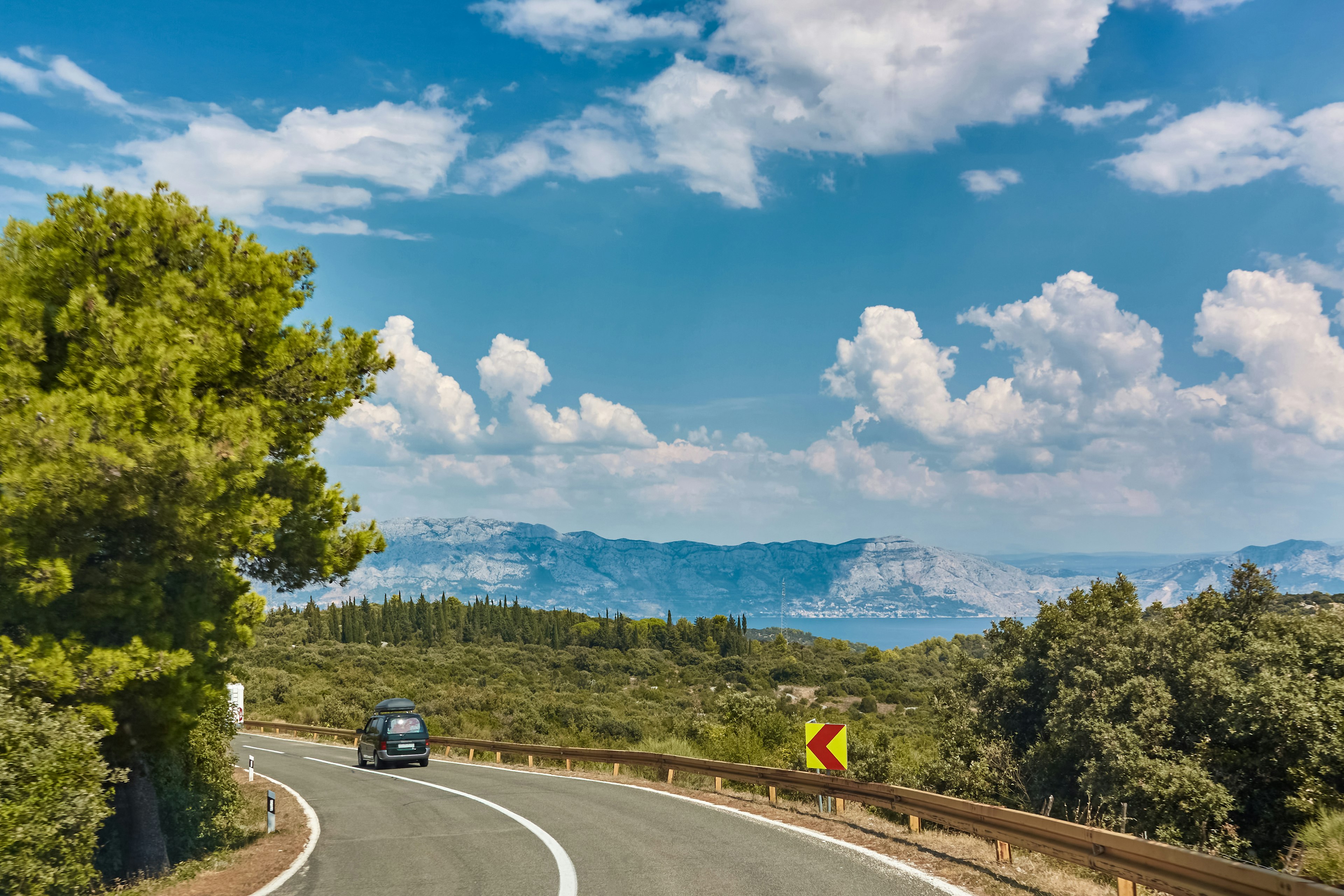 A car drives along a coastal road with island scenery stretching out in the distance