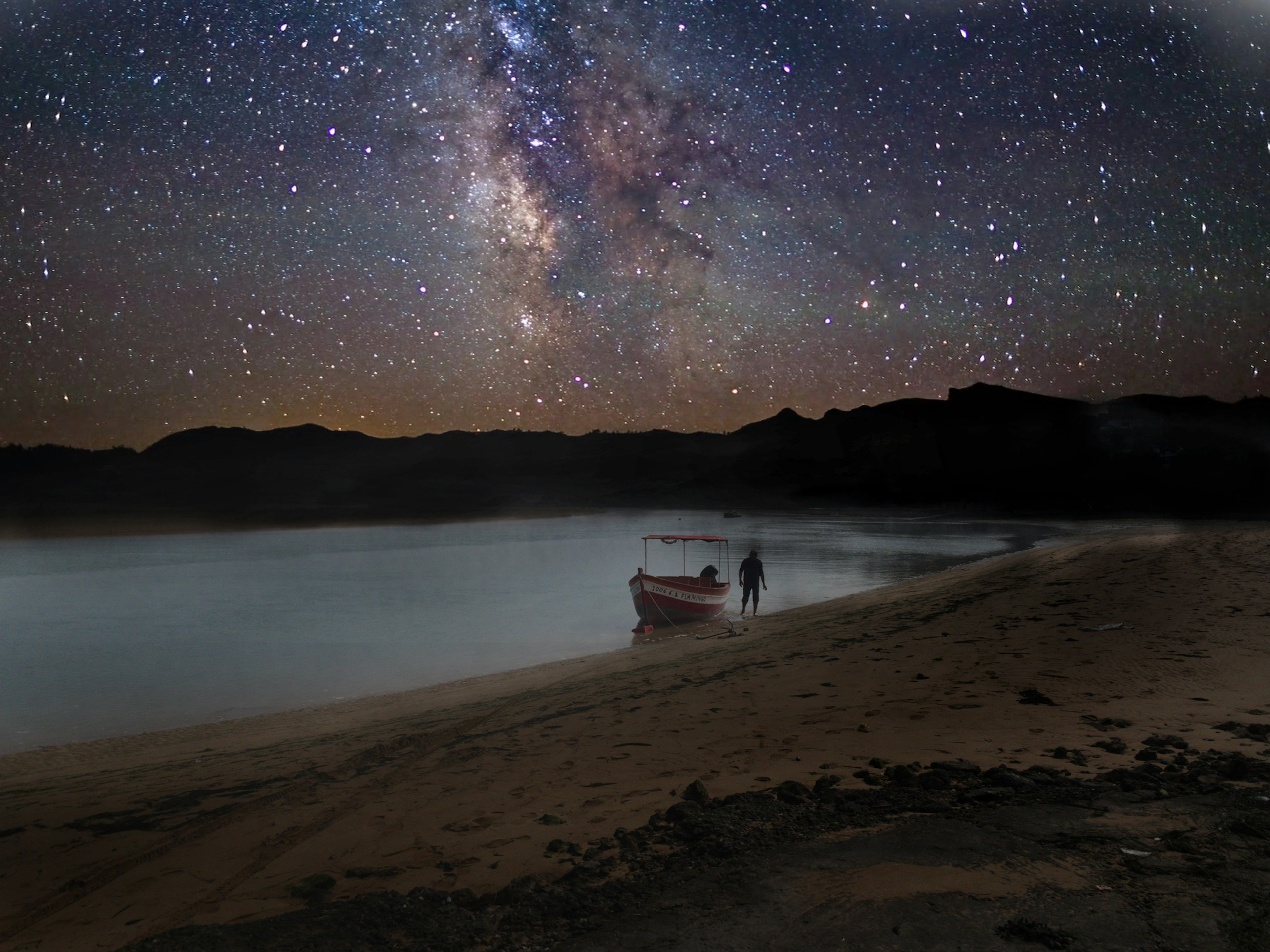 Under a blanket of sparkling night-time stars, a man walks near a fishing boat that's bobbing on the sea at Oualidia in Morocco