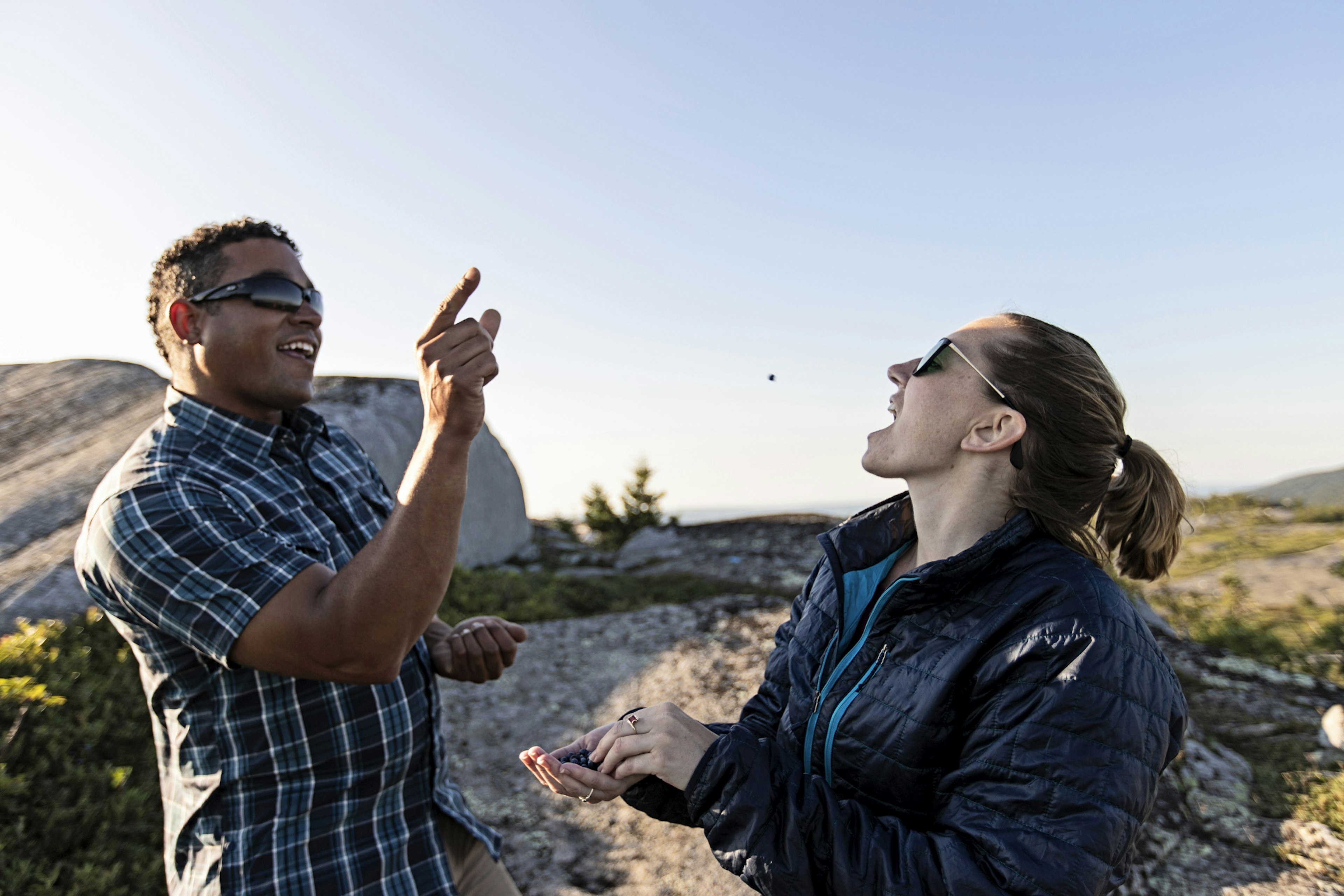 A man throws a blueberry towards a woman who attempts to catch it in her mouth