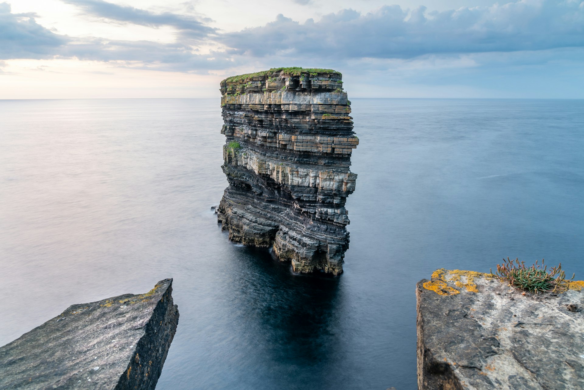 Sea stack standing in the ocean framed by other rocks on the cliff