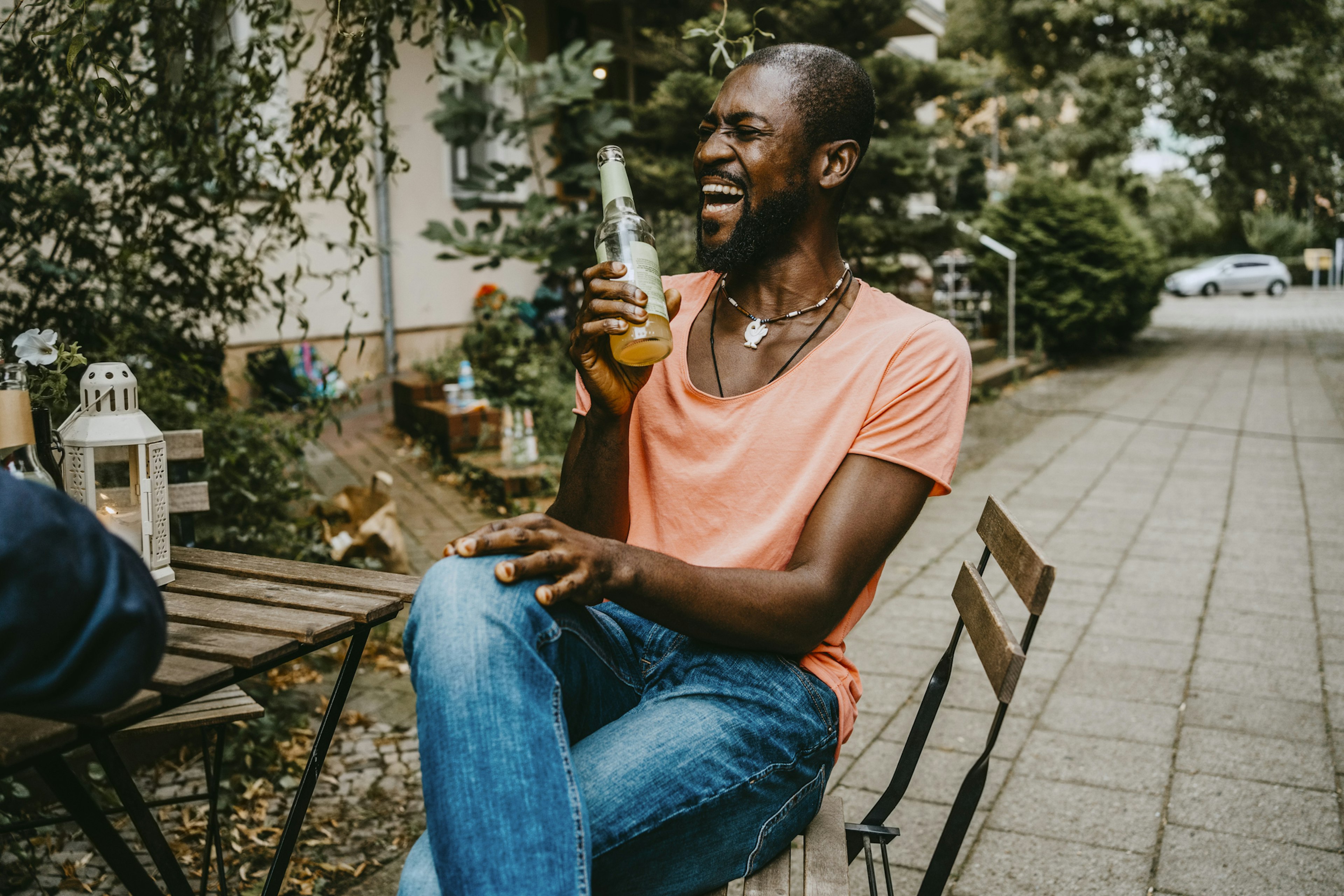 Happy man laughing while having beer at table on footpath