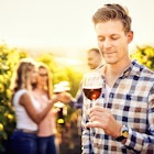 Portrait of a young, millennial vintner holding and smelling a glass of organic bio red wine outdoors in a vineyard with his friends in the background - Vine-growing, and wine-tasting concept
1368812551