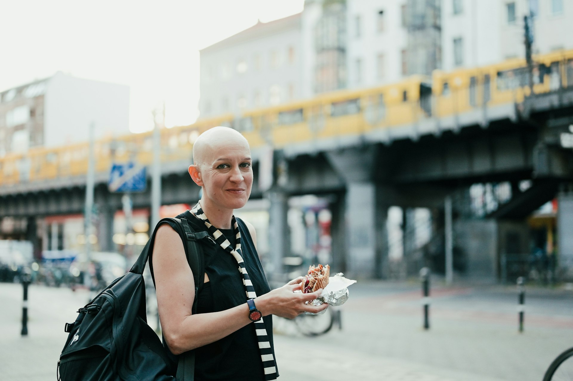 A woman with a shaven head eating a doner kebab on the street in Berlin
