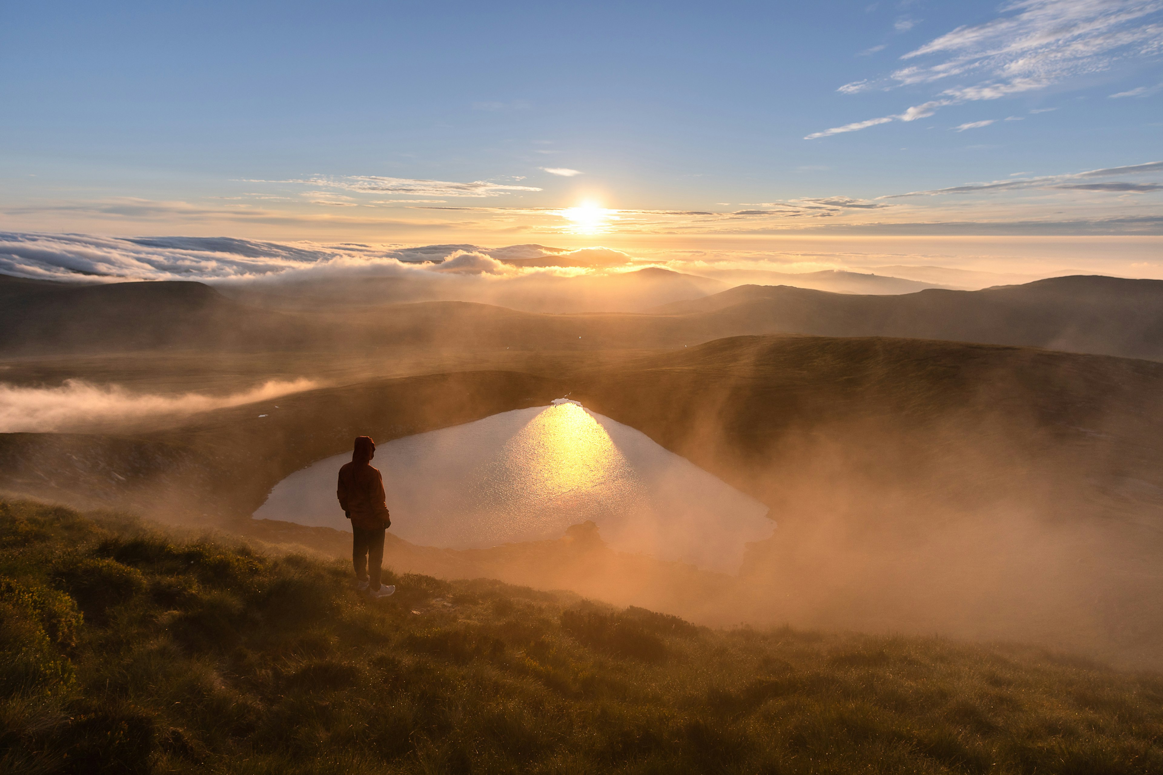 A hiker stands on a hilltop overlooking a heartshaped lake