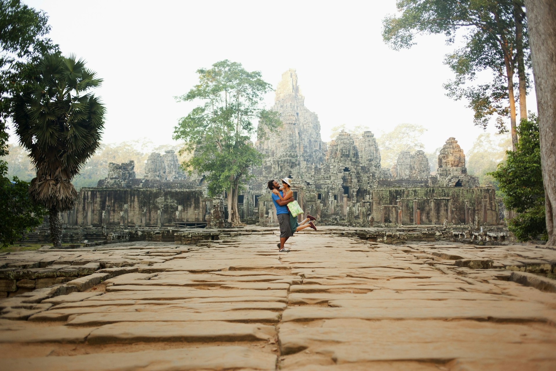 A man lifts a woman into an embrace in front of the vast ancient jungle temple of Angkor in Cambodia