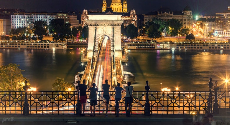 Five people looking out over Széchenyi Chain Bridge in Budapest, Hungary, at night.
