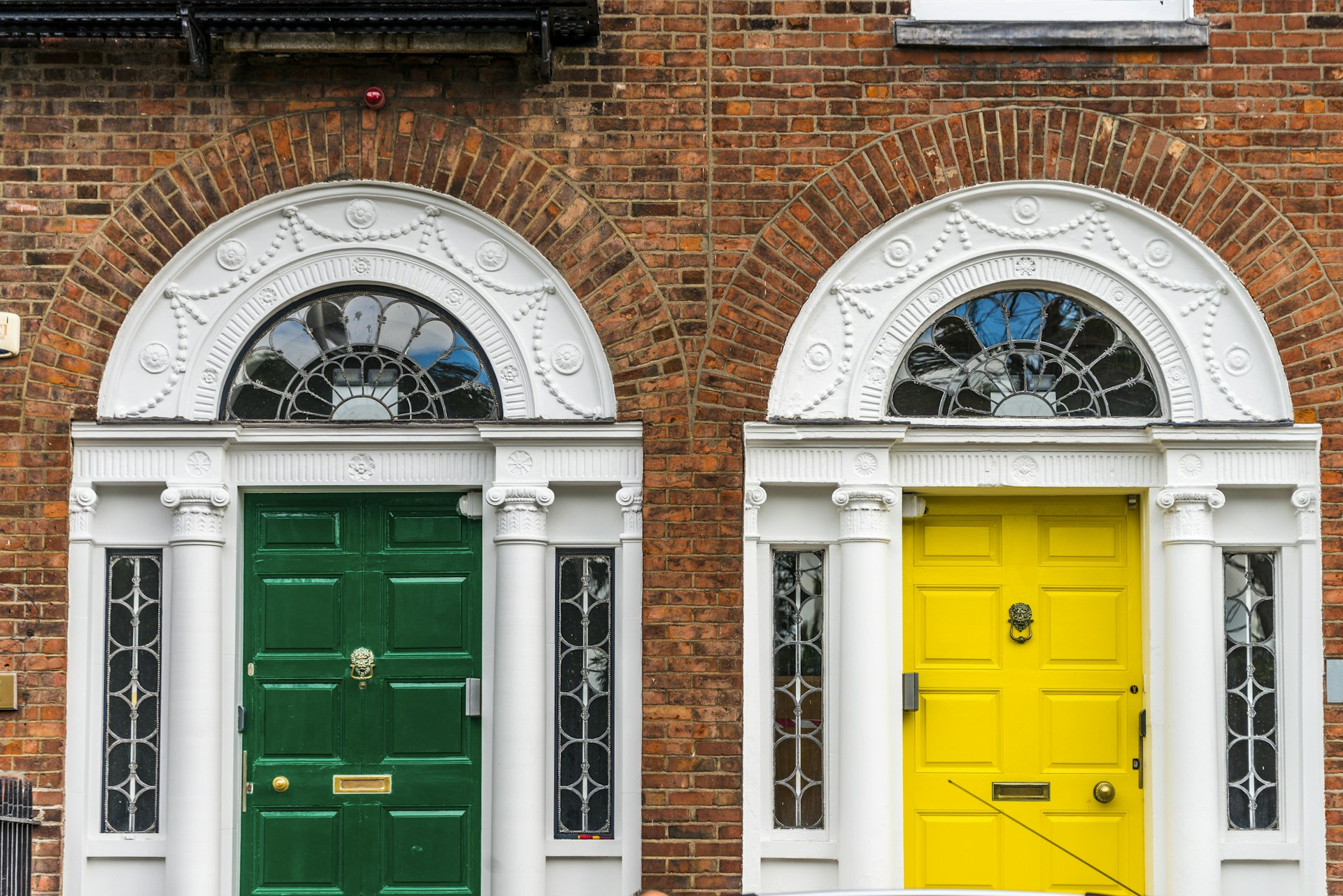 A Georgian-style green door and a yellow door in the front of a red-brick building
