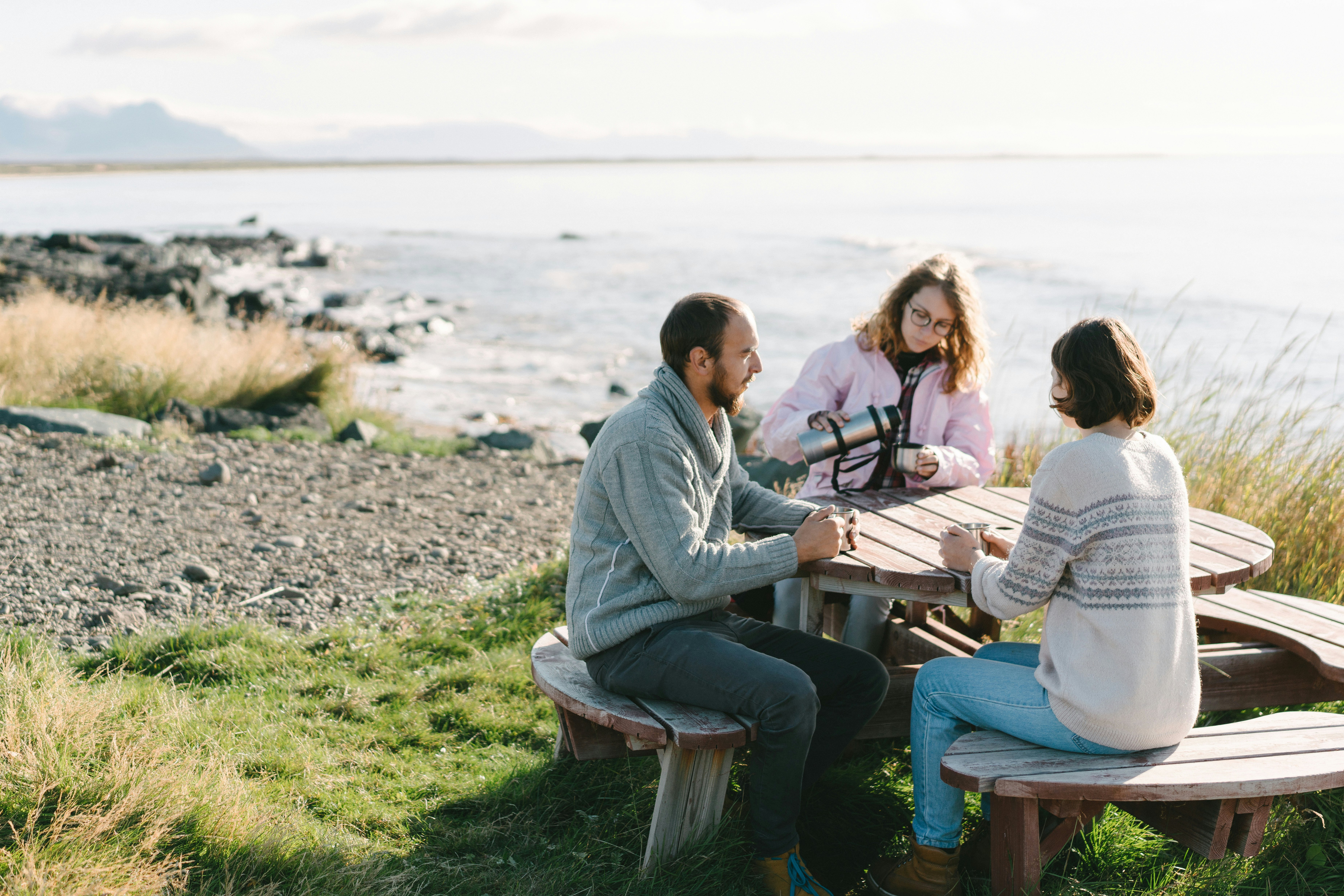 People sit at a table on a beach in Iceland pouring drinks from a flask