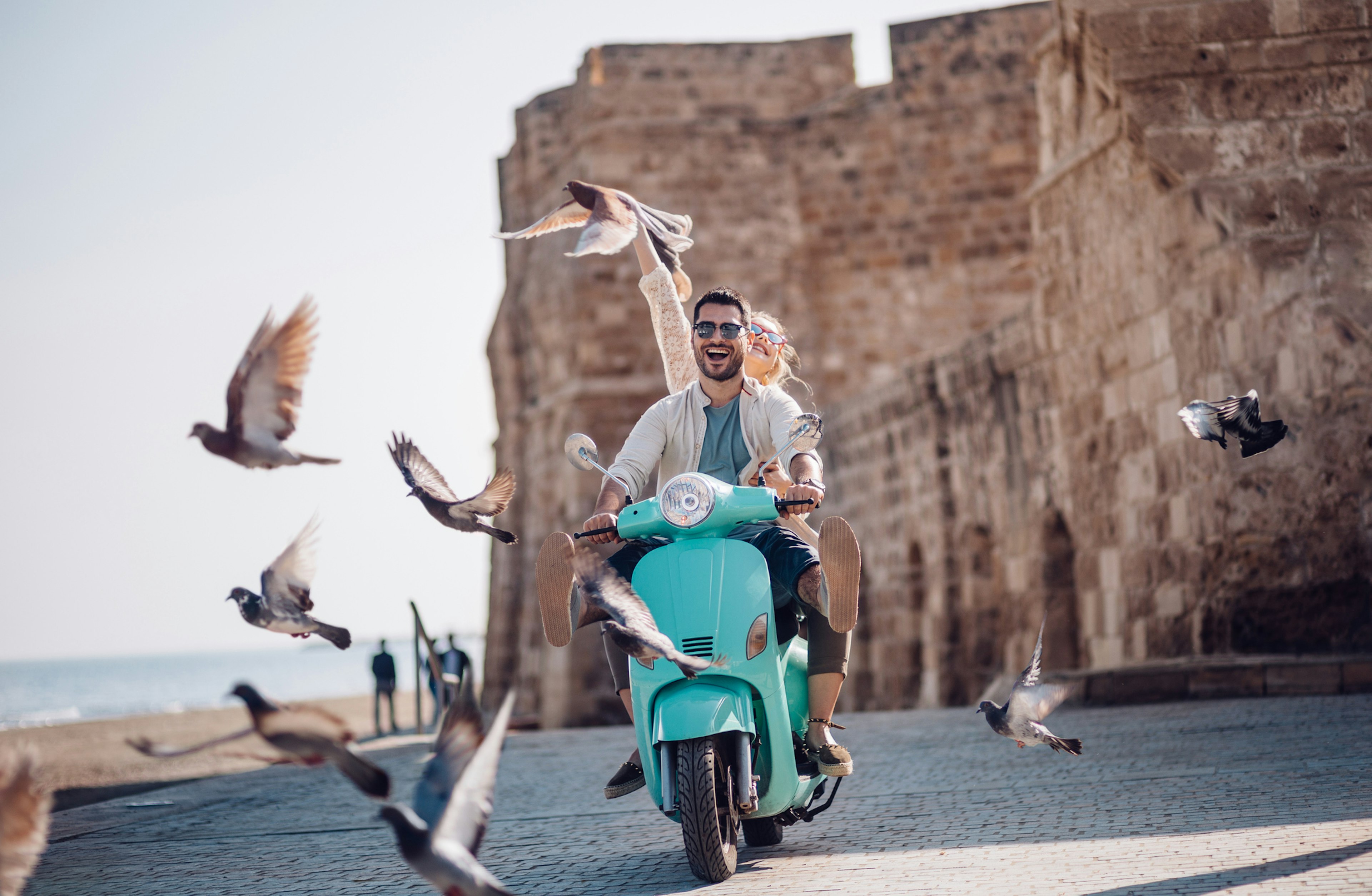 Tourist friends on summer holidays in Europe having fun riding retro scooter by the sea