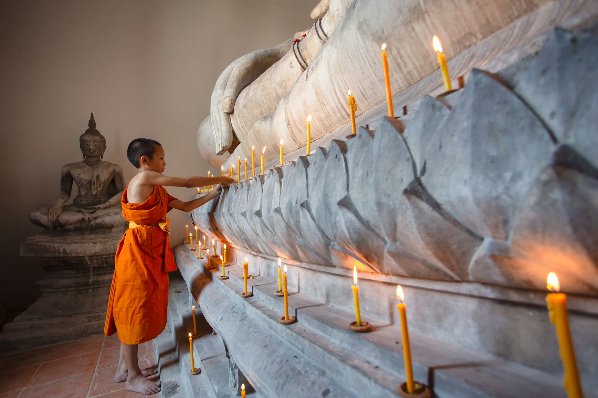 A young monk worships the Buddha with candle and light at Wat Phutthai Sawan, Ayuthaya, Thailand