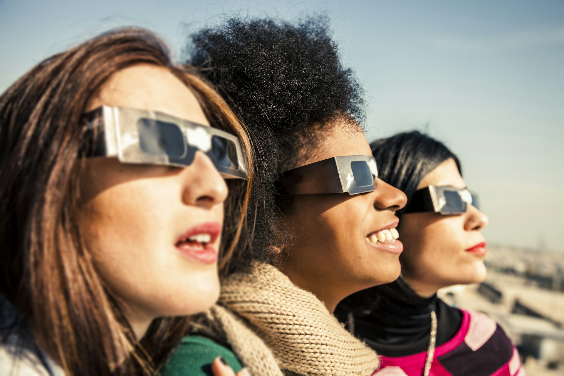 Tres mujeres con gafas miran al cielo durante un eclipse solar