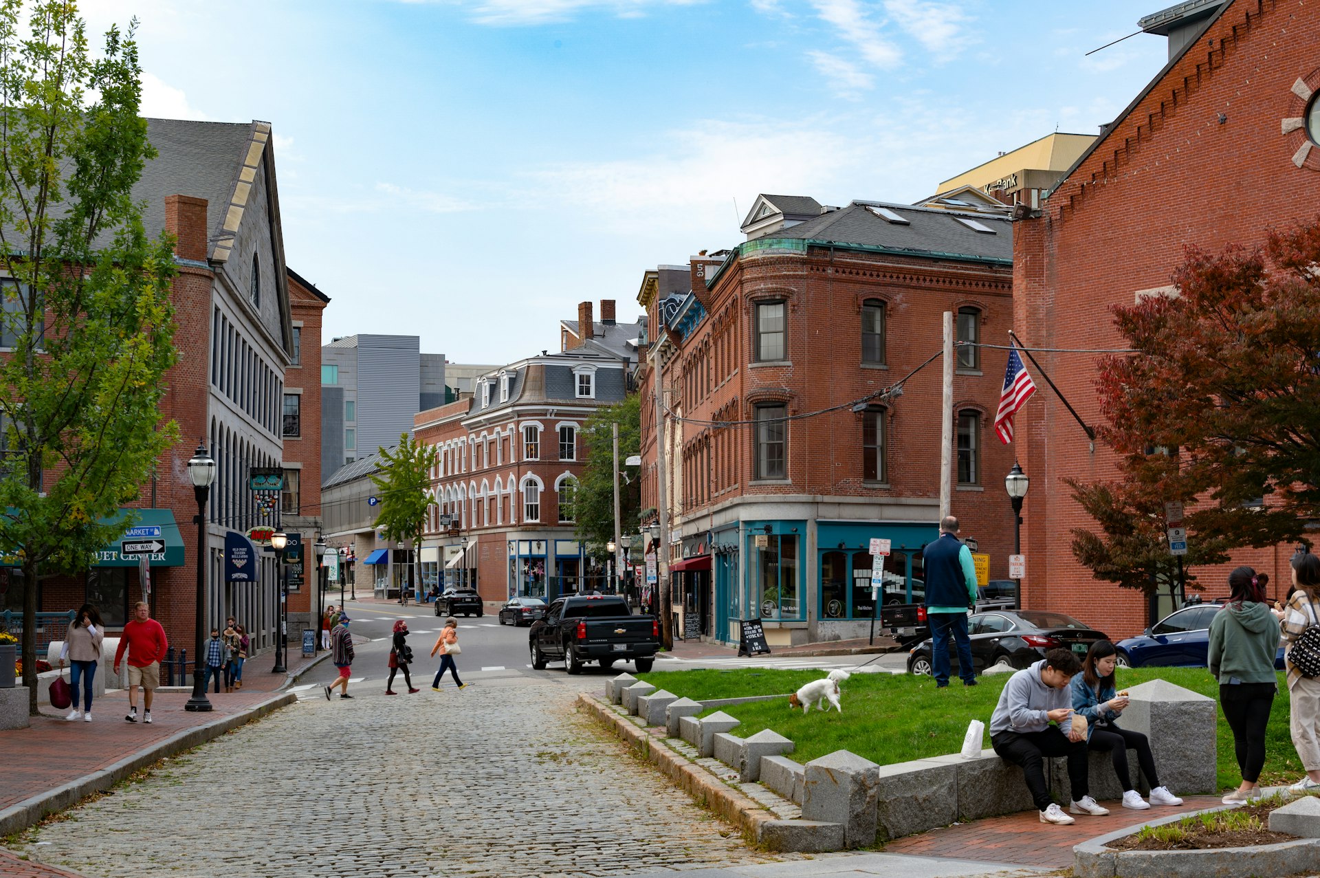 People walking around and hanging out in the Historic Waterfront District of Portland, Maine, with cobblestone streets and red-brick buildings.