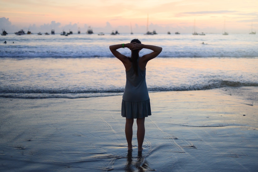 女人在沙滩上戴着双手支撑头部的衣服。该女人在尼加拉瓜圣胡安·德尔·苏尔（San Juan del Sur）的日落期间脚踩在水中。555761647妇女的妇女在海滩上戴着双手支撑头部。该妇女在尼加拉瓜圣胡安·德尔苏尔的日落期间脚踩在水中。