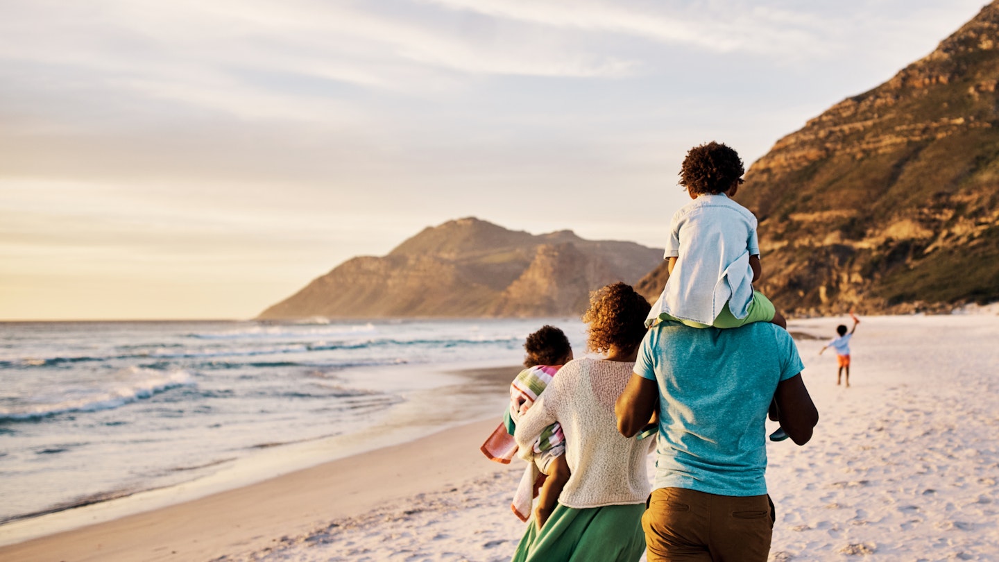 Rear of a family walking on the beach with copy space. African parents with little kids bonding and strolling by ocean. Little children enjoying the outdoors during their summer holidays or vacation 1408174631