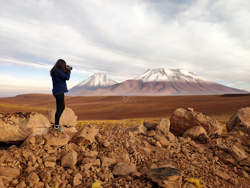 Silhouette of a tourist woman photographing Licancabur and Juriques volcanoes in the border between Chile and Bolivia