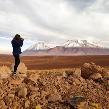 Silhouette of a tourist woman photographing Licancabur and Juriques volcanoes in the border between Chile and Bolivia