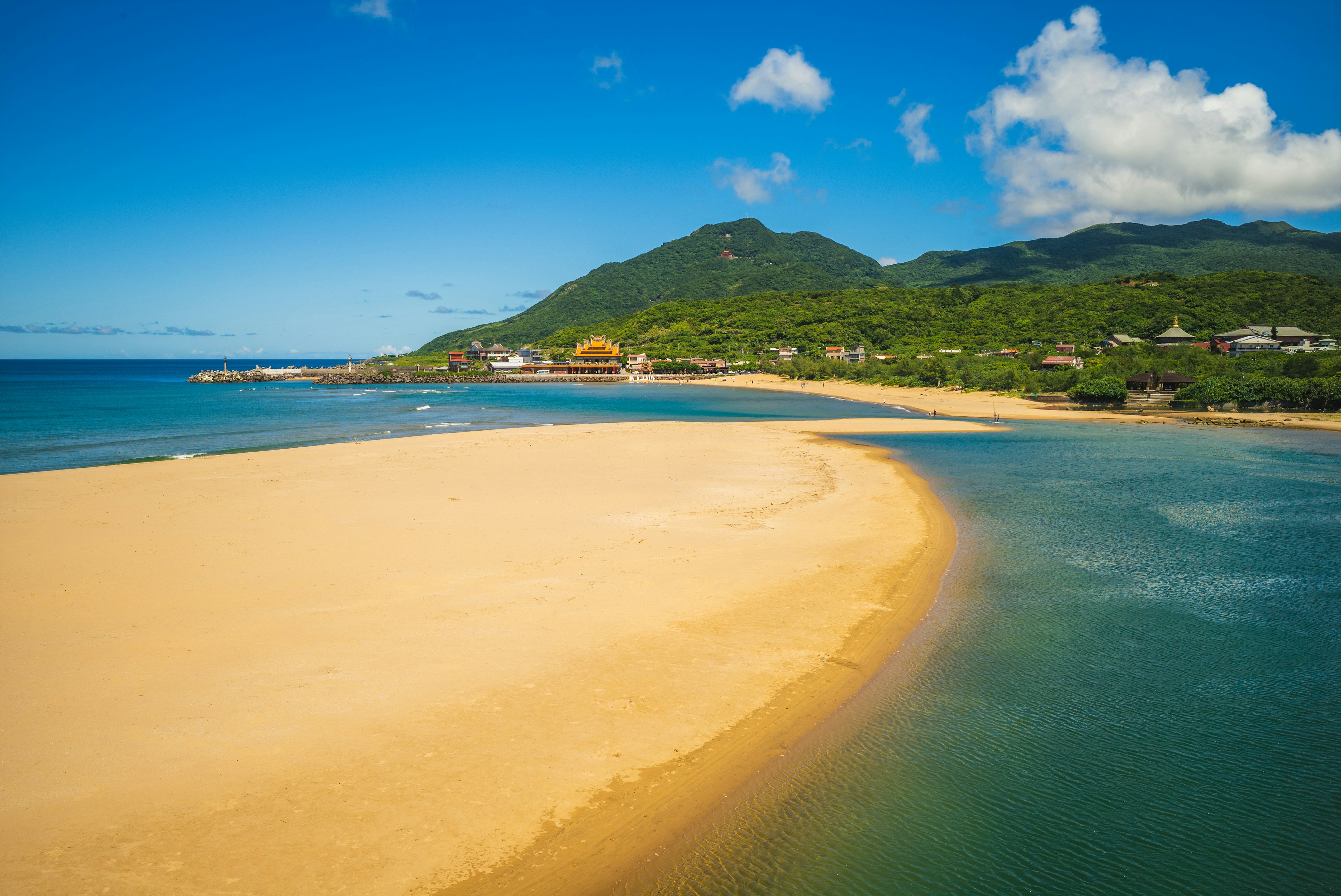 A golden sandbar with a peak in the distance and ocean lapping it at from either side