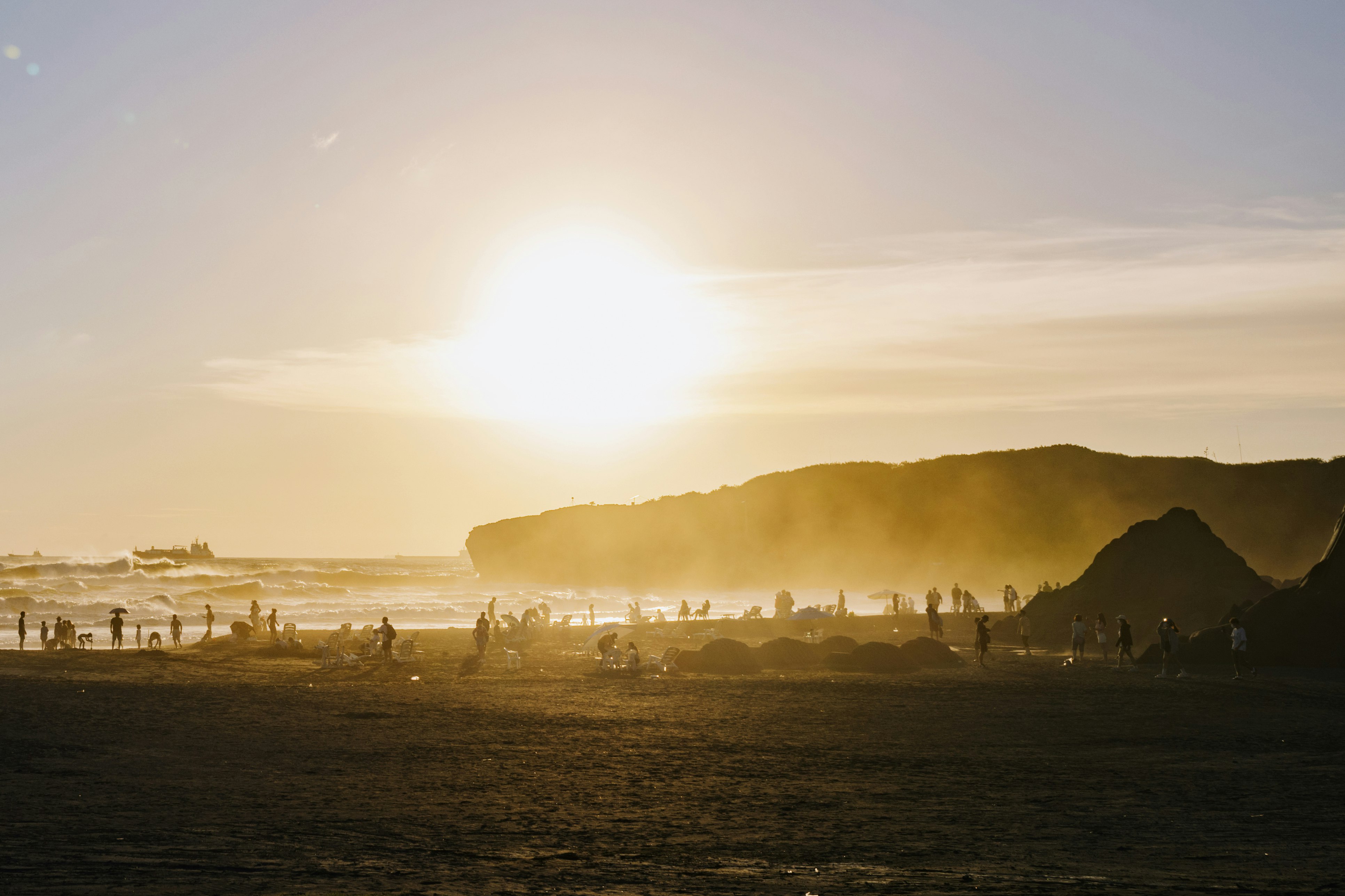 Crowds on the beach are silhouetted as the sun sets, streaking orange across the sky