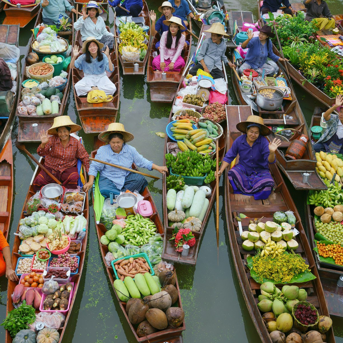 Crowded wooden boats in canal with fruits, vegetables, foods and grocery products for sell and trade by villagers at Tha Kha traditional floating market.