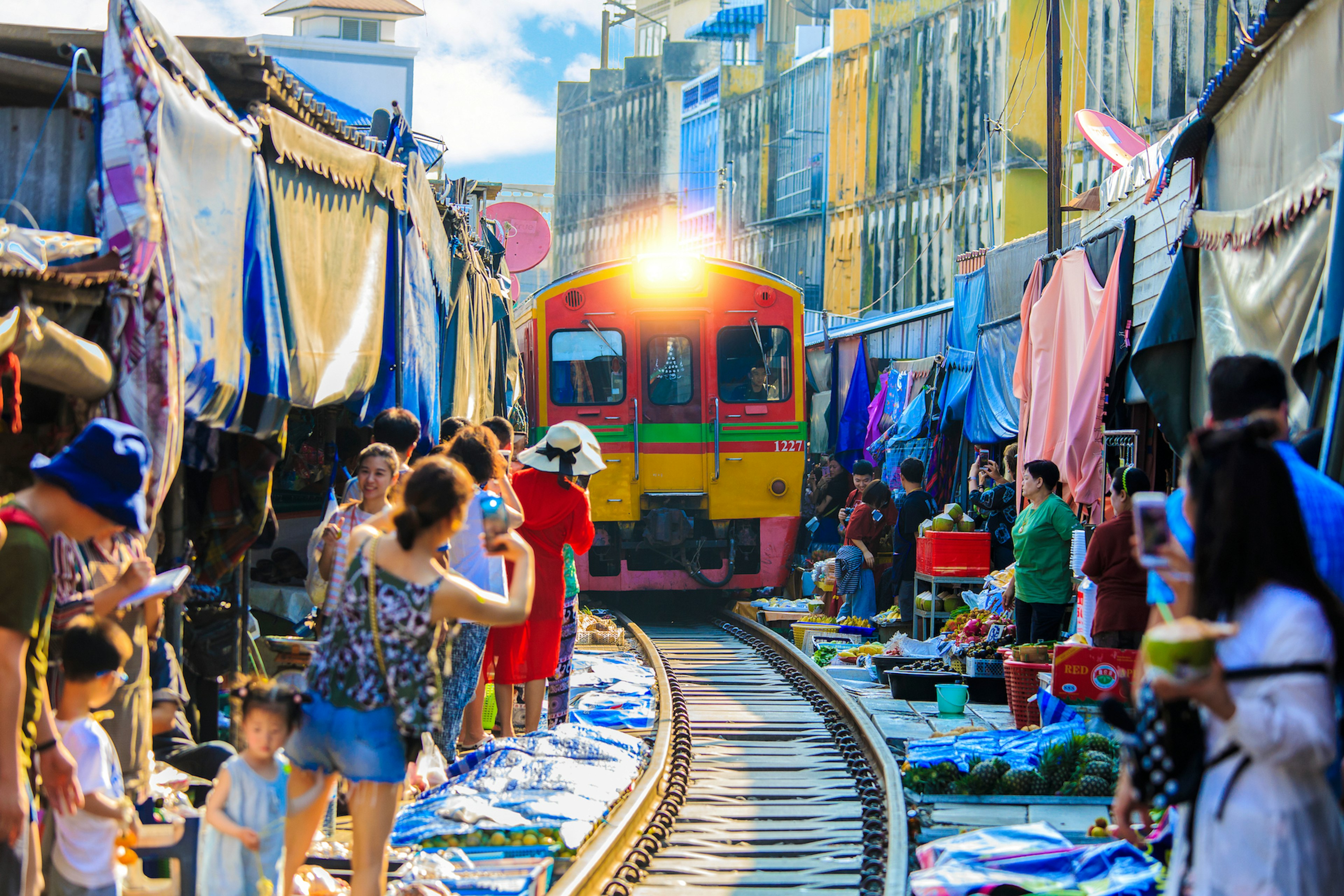 A trainline with a market either sides of the tracks with a train on the approach. People holding cell phones take photos from the side of the tracks