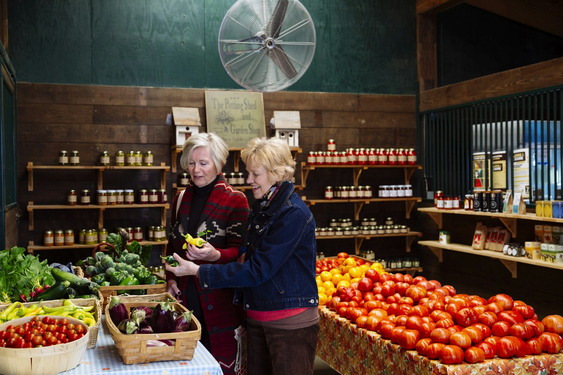 Two women browse for goods in a farm store with walls lined with produce