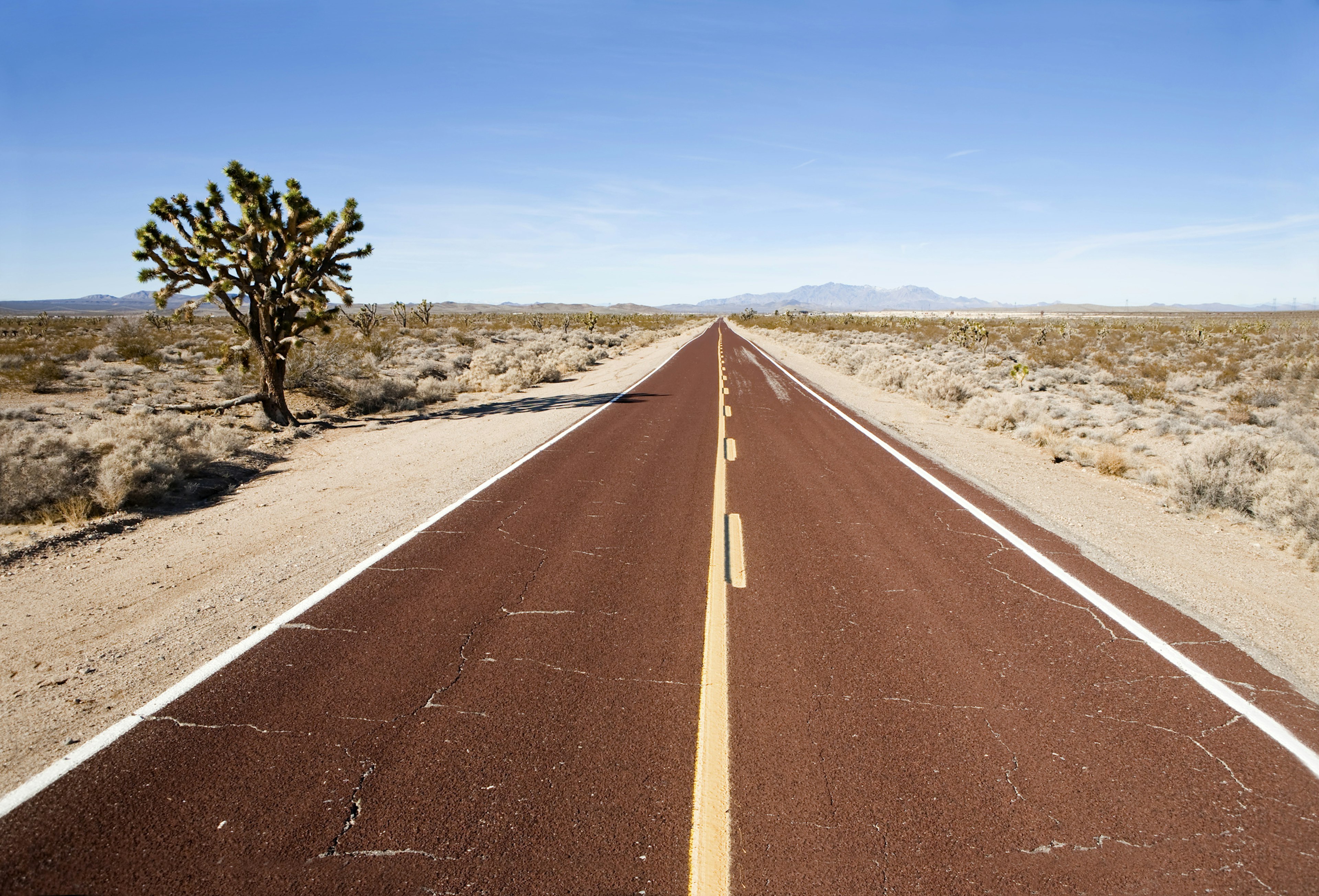 A long straight red paved road through a desert landscape