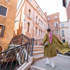 Young woman walking beautiful streets at water canals in Venice. Concept of happy vacations in Italy. Caucasian stylish woman in coat with colorful shawl Young woman walking beautiful streets at water canals in Venice. Concept of happy vacations in Italy. Caucasian stylish woman in coat with colorful shawl