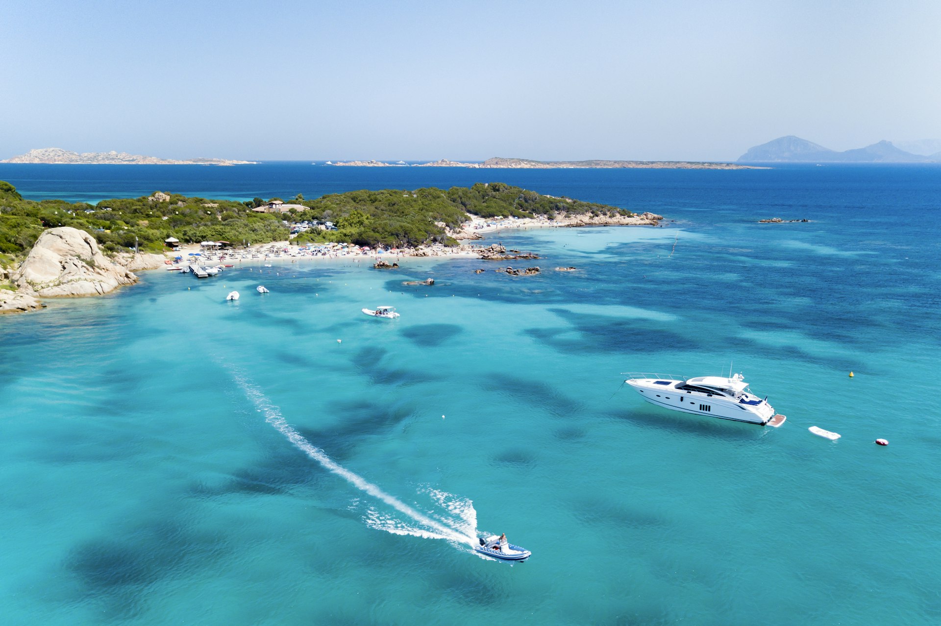 View from above, aerial view of an emerald and transparent mediterranean sea with a white beach and some boats and yachts. Costa Smeralda, Sardinia, Italy.
