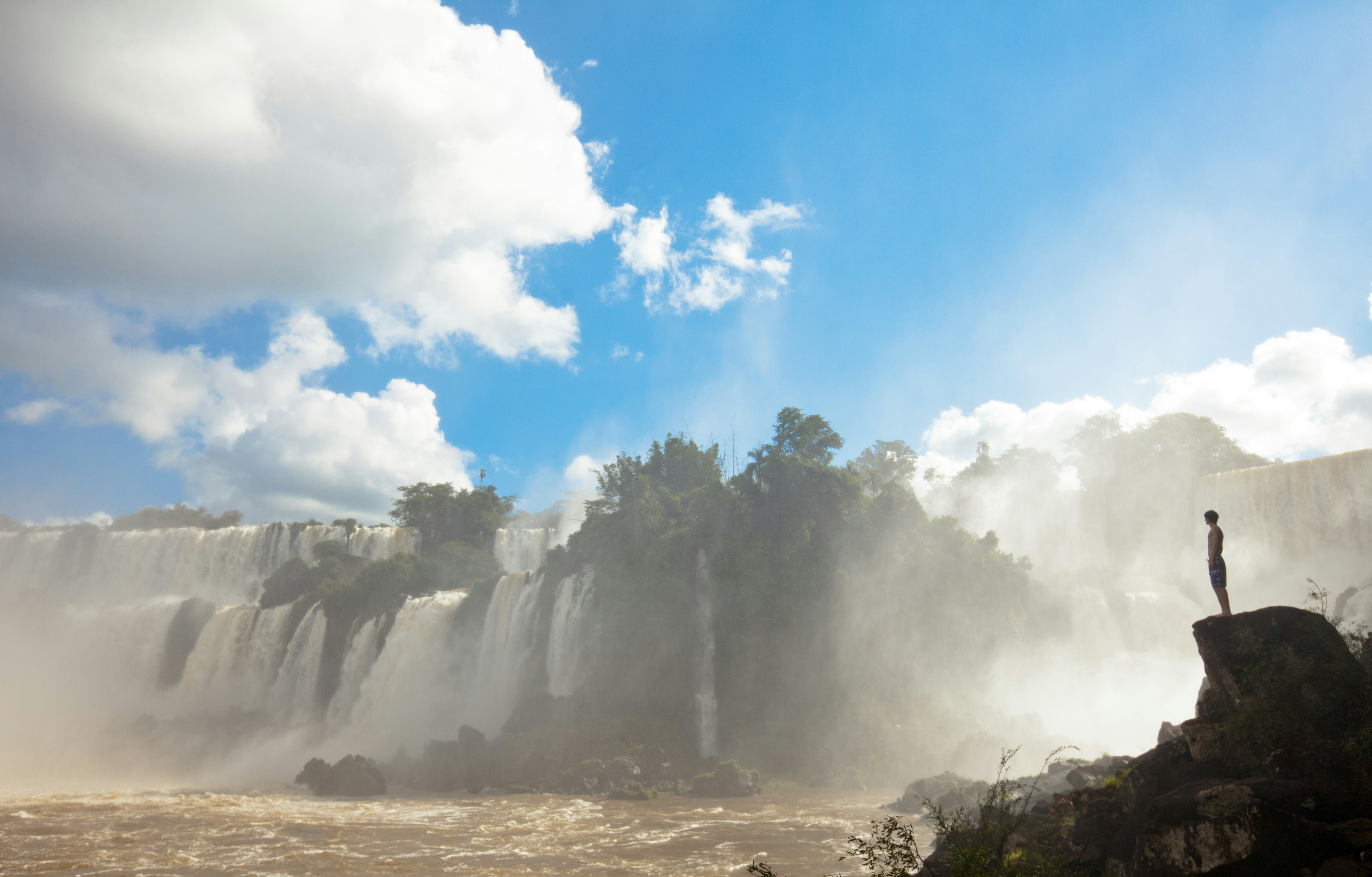 A young man sits on the edge of Iguazú Falls, admiring the power and strength of water in this majestic place of natural beauty