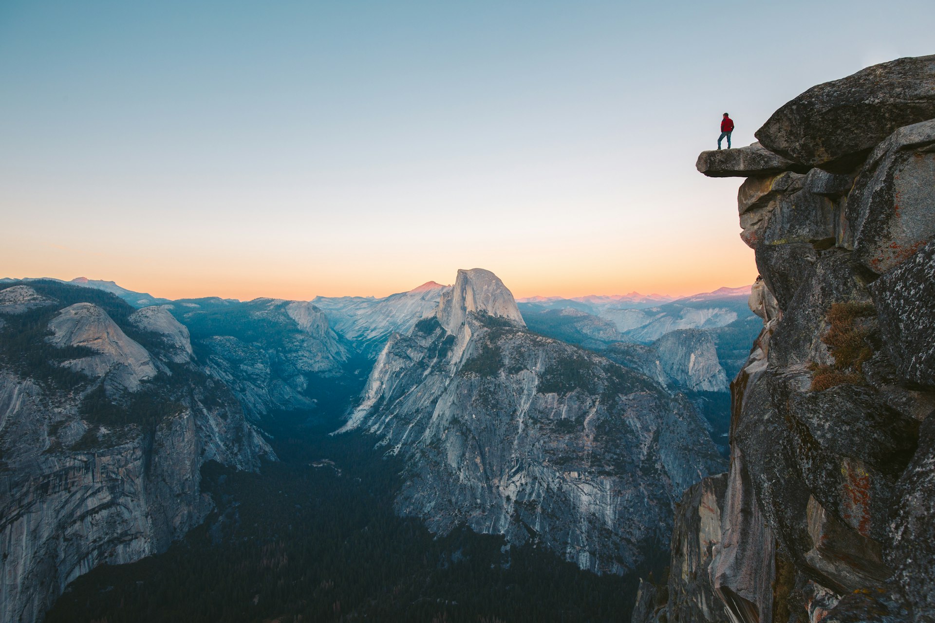 Hiker standing on an overhanging rock and taking in the view at Glacier Point overlook during the evening