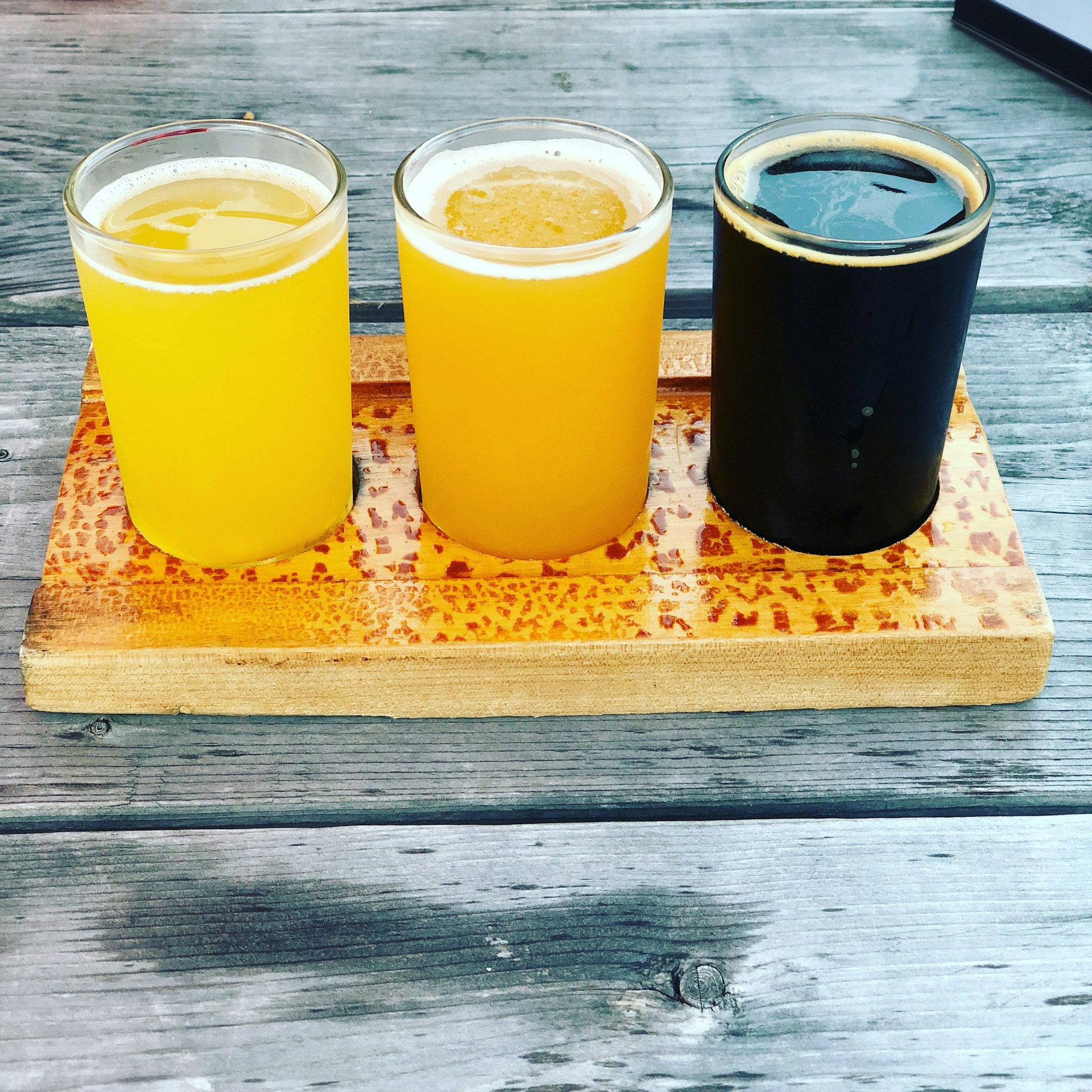 A flight of three craft beers standing on a wooden panel
