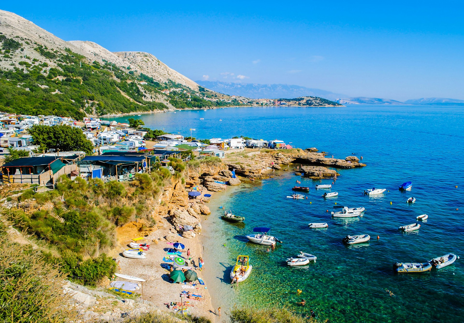 High-angle view of a campground, sunbathers and boats at Stara Baska beach, Krk, Croatia