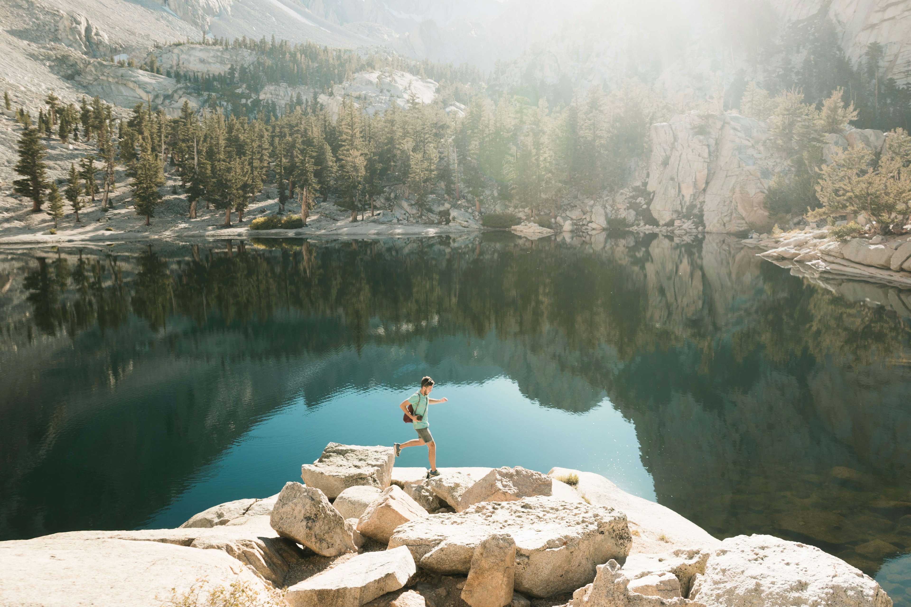 A young sporty man runs and jumps on the rocks next to a lake