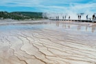 Tourists walking around the Grand Prismatic spring in Yellowstone National Park, low-angle view with mud and shallow water in the foreground
