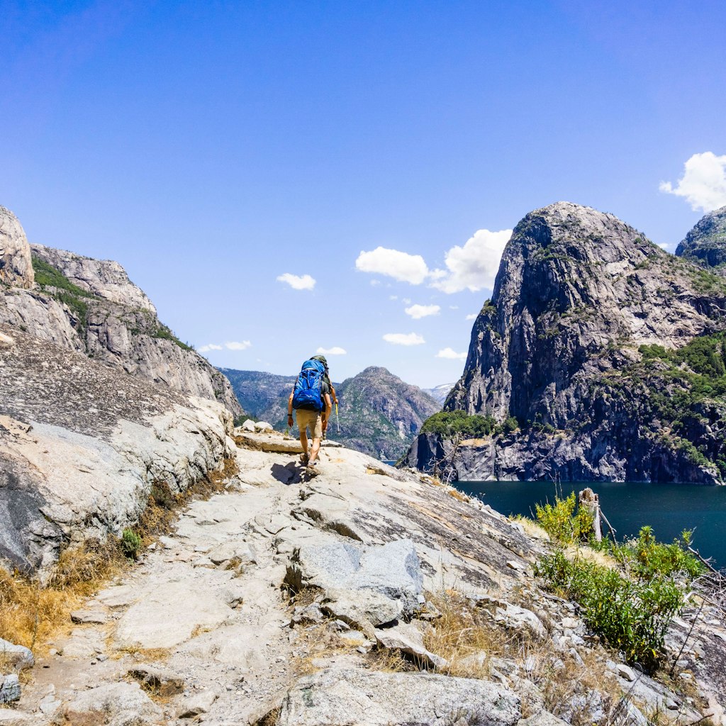 A person seen from behind, hiking on the shoreline of Hetch Hetchy reservoir in Yosemite National Park, Sierra Nevada mountains, California. The reservoir is one of the main sources of drinking water for the San Francisco bay.