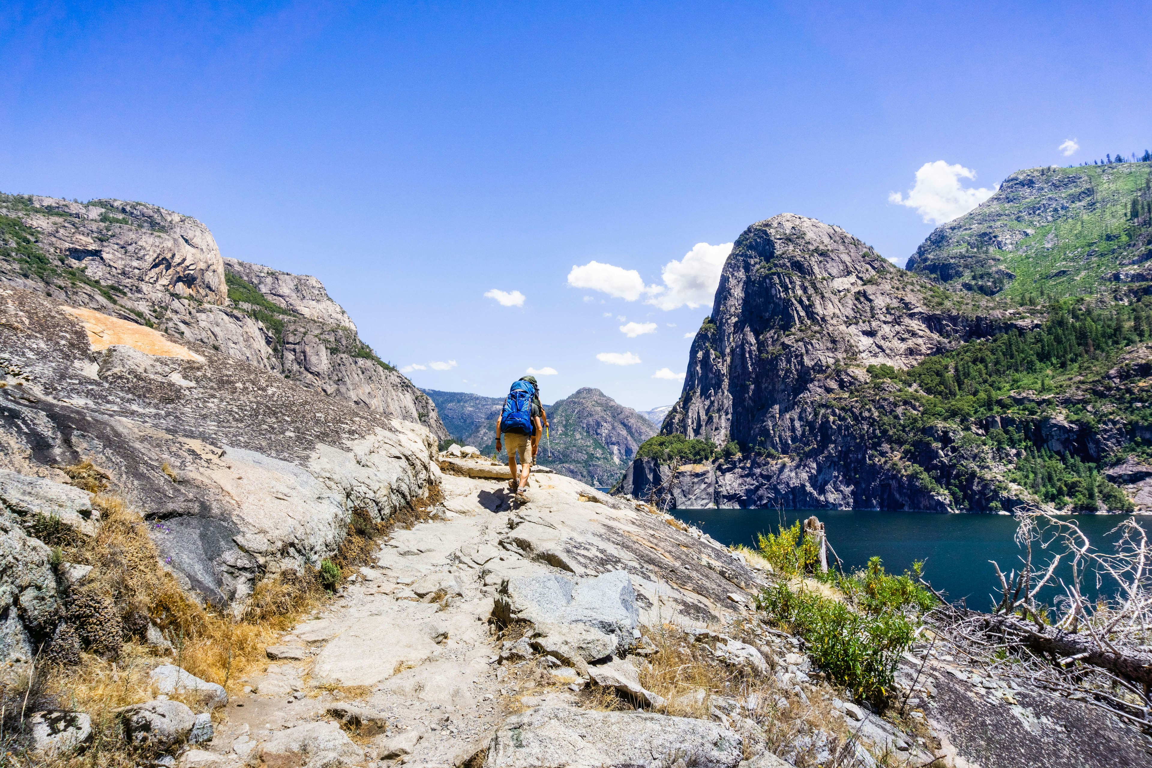 A person seen from behind, hiking on the shoreline of Hetch Hetchy reservoir in Yosemite National Park, Sierra Nevada mountains, California. The reservoir is one of the main sources of drinking water for the San Francisco bay.