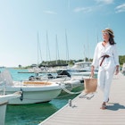 Young pretty woman in white summer clothing walking by yachts docked in Istria, Croatia.