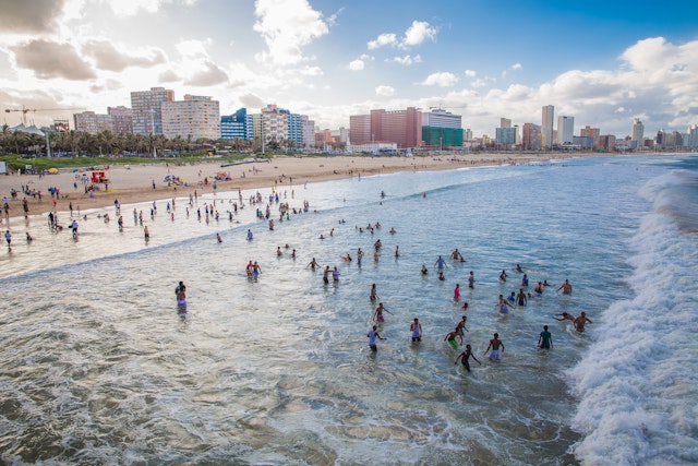 Many people splashing in the ocean on a long stretch of golden beach