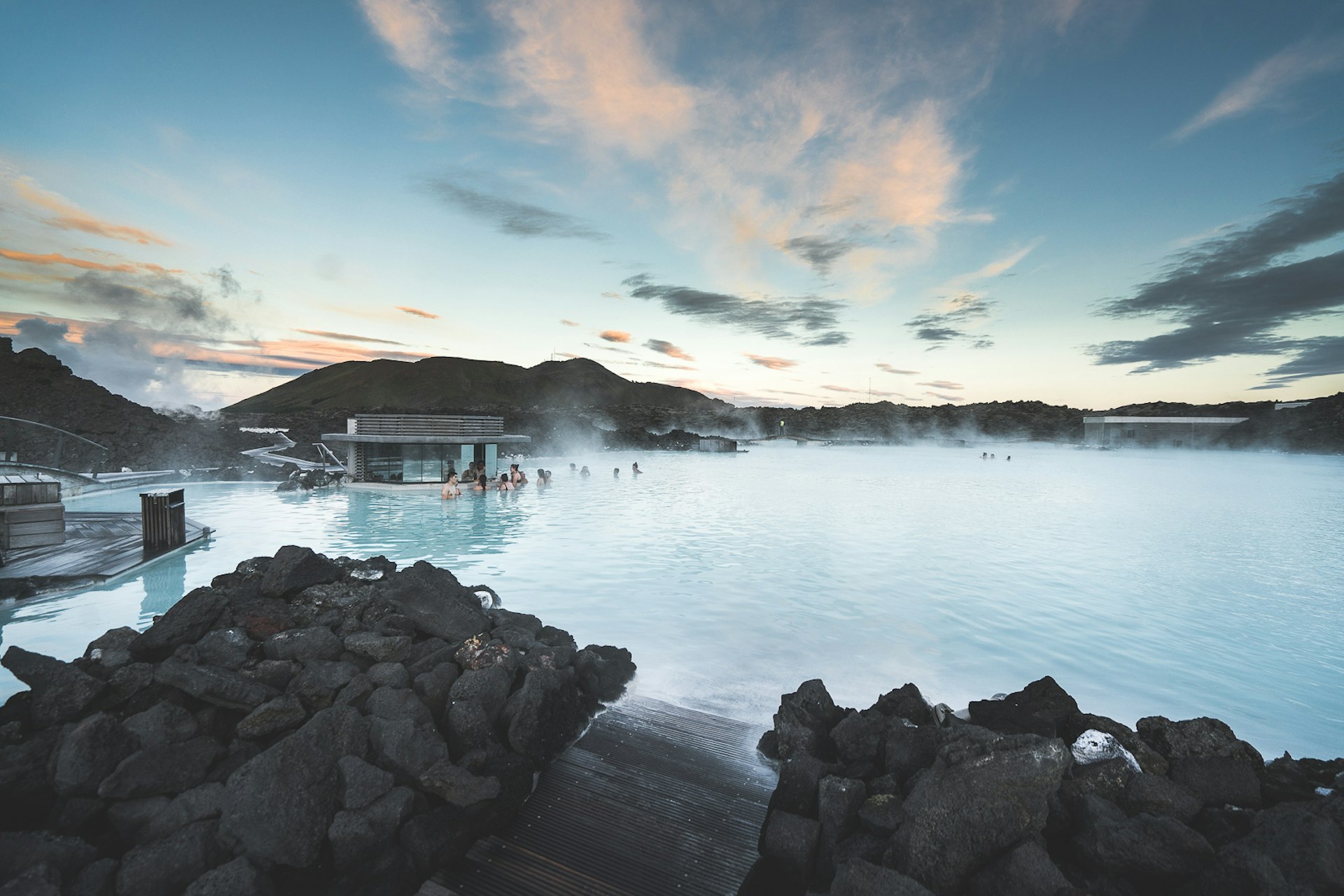 People enjoying the Blue Lagoon in Iceland, surrounded by rocky mountains 