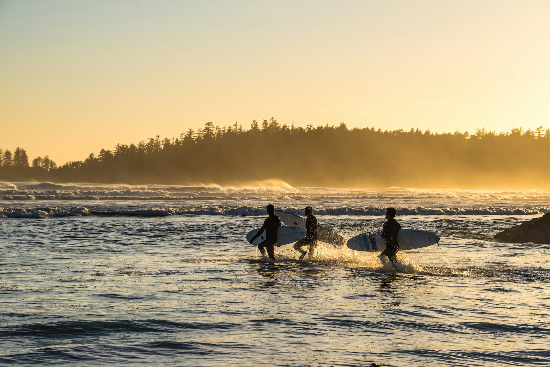 Surfers running out to catch some waves during sunset on Long Beach, a very popular Canadian surf spot. 