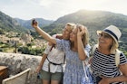 Multi generation family sightseeing beautiful town of Valldemossa. Sunny summer day in Majorca, Spain...Teenage girl, mother and grandmother are taking selfies. Behind them there is a magnificent view of the town of Valldemossa and the surrounding mountains - Serra de Tramuntana...Canon R5
1346146237