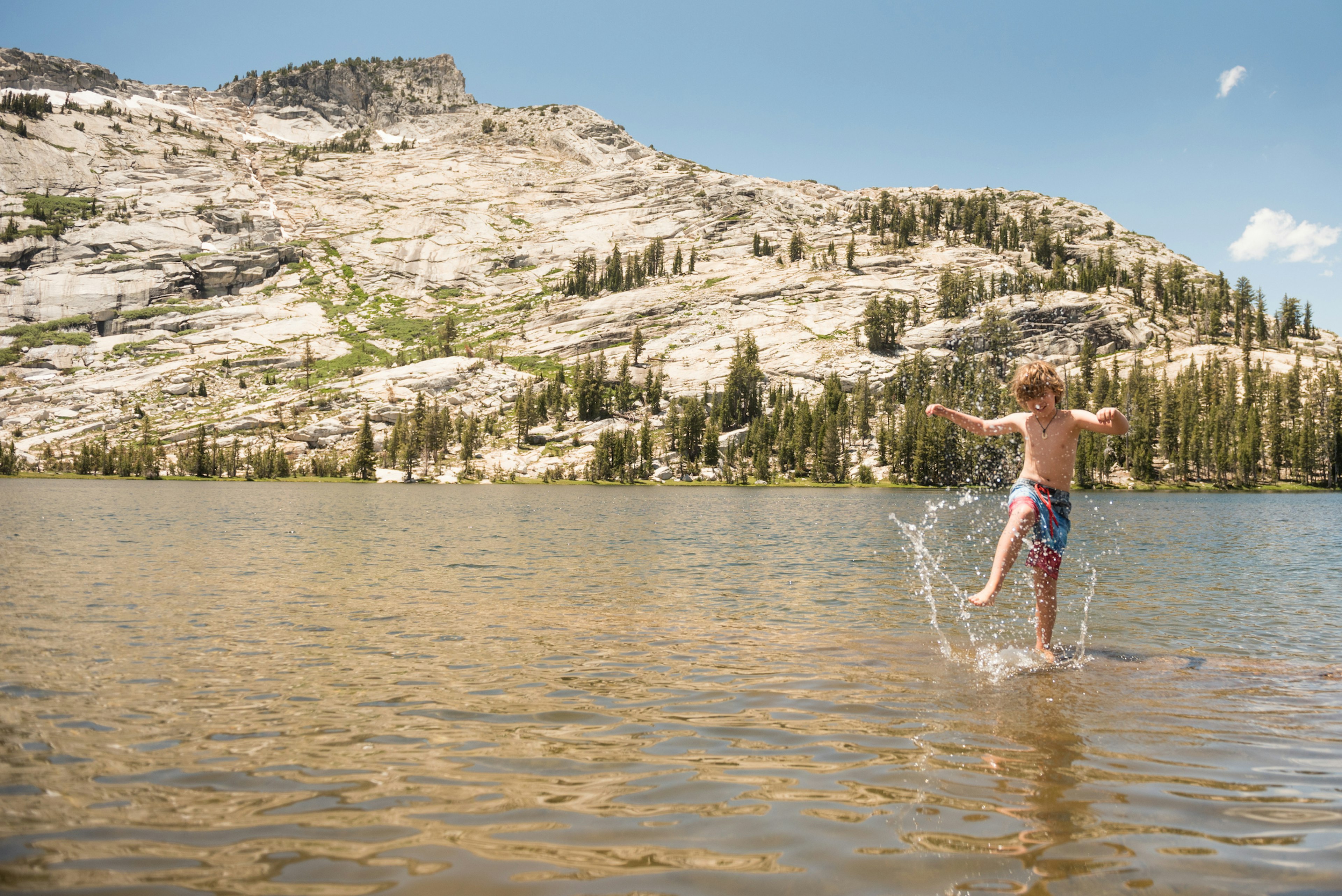 A child splashes in the shallows of a lake surrounded by hills