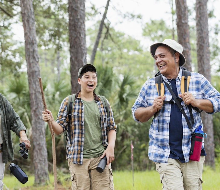 A multi-generation Hispanic family hiking together outdoors in the woods, wearing plaid shirts and hats and carrying walking sticks. The 12 year old boy walking in the middle, behind his father, a mature man in his 50s, and in front of his grandfather, a senior man in his 80s.
1129648546
hiking, healthy lifestyle, leisure activity, public park, natural parkland, woodland, nature, exploration, discovery, summer, springtime, outdoors, casual clothing, plaid shirt, hat, hiking pole, three people, senior men, mature men, boys, latin american and hispanic ethnicity, child, 12-13 years, 50-54 years, 80-89 years, vitality, active seniors, multi-generation family, father, son, grandfather, grandson, togetherness, bonding, friendship, smiling, happiness, cheerful, relaxation, candid, walking, talking, laughing, real people, waist up, florida - us state, adventure, retirement, sc0993