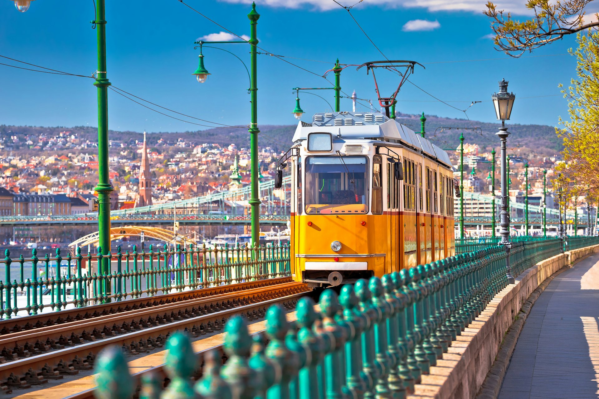 A yellow tram runs along the riverside in Budapest coming towards the camera