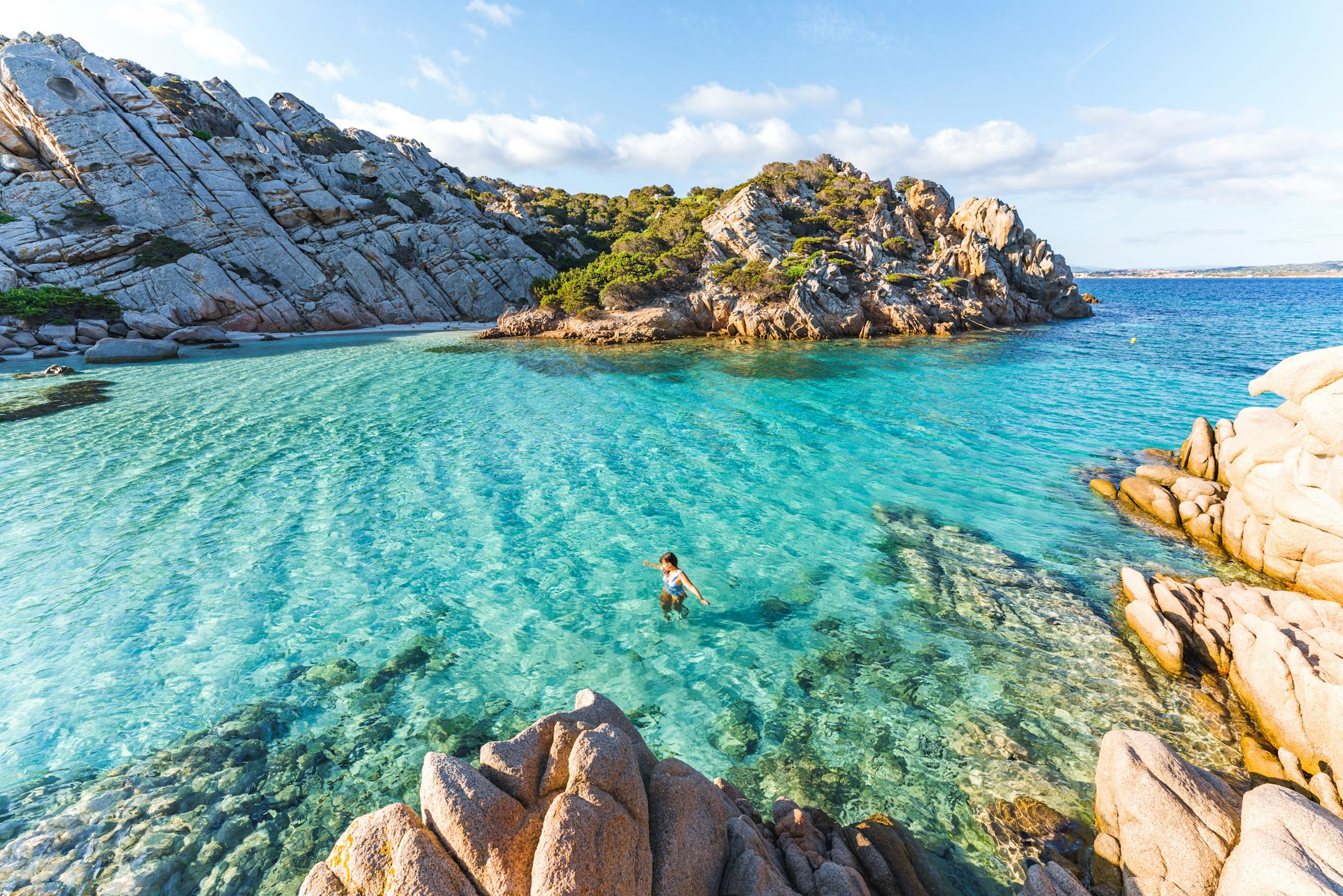 A person swims in the water in a secluded cove at the beach of Cala Napoletana, Sardinia. 