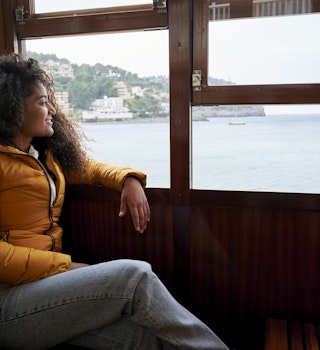 Woman in train looking out the window at the sea
1395582553
A woman smiling and looking out the window at the sea view in Spain